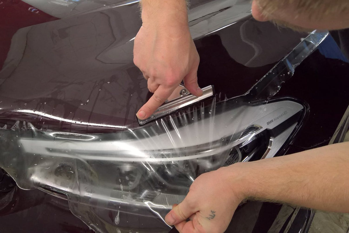 Installer applying paint protection film to a car headlight